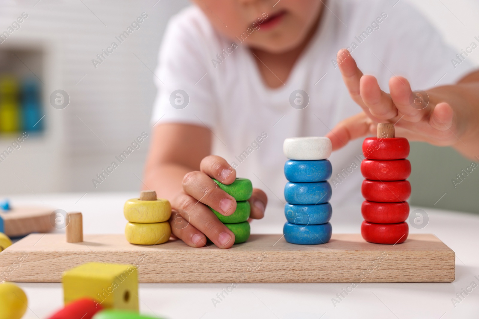 Photo of Motor skills development. Little boy playing with stacking and counting game at table indoors, closeup