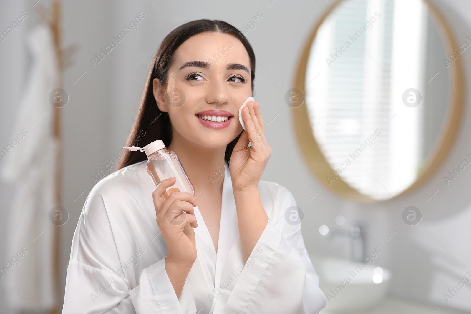 Photo of Beautiful woman removing makeup with cotton pad indoors