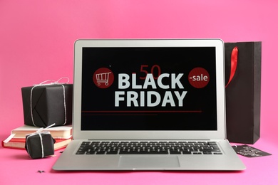 Photo of Laptop with Black Friday announcement, notebooks and gifts on pink background