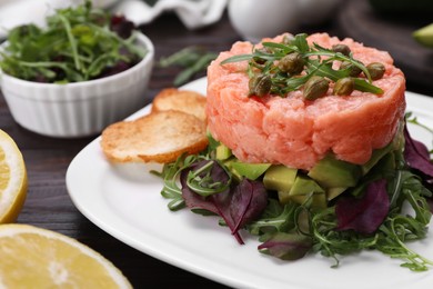 Photo of Tasty salmon tartare with avocado, greens and croutons on wooden table, closeup