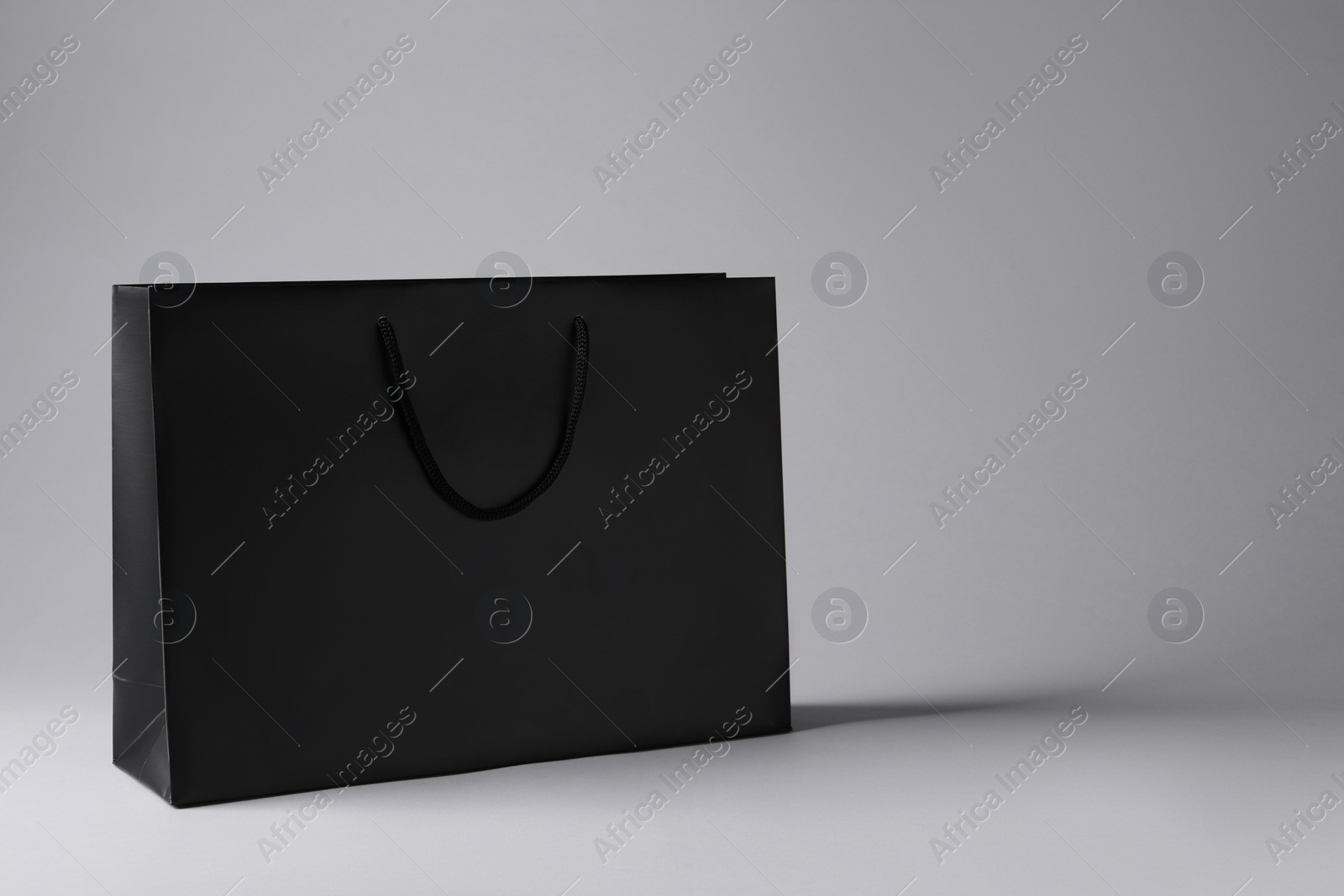 Photo of Black paper bag on light grey background, space for text