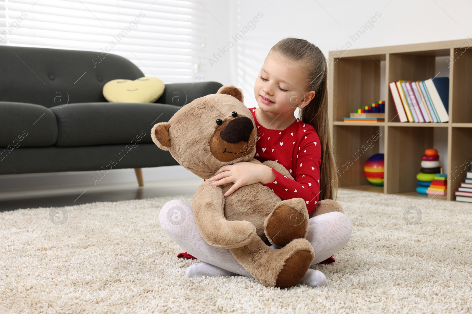 Photo of Cute little girl playing with teddy bear at home