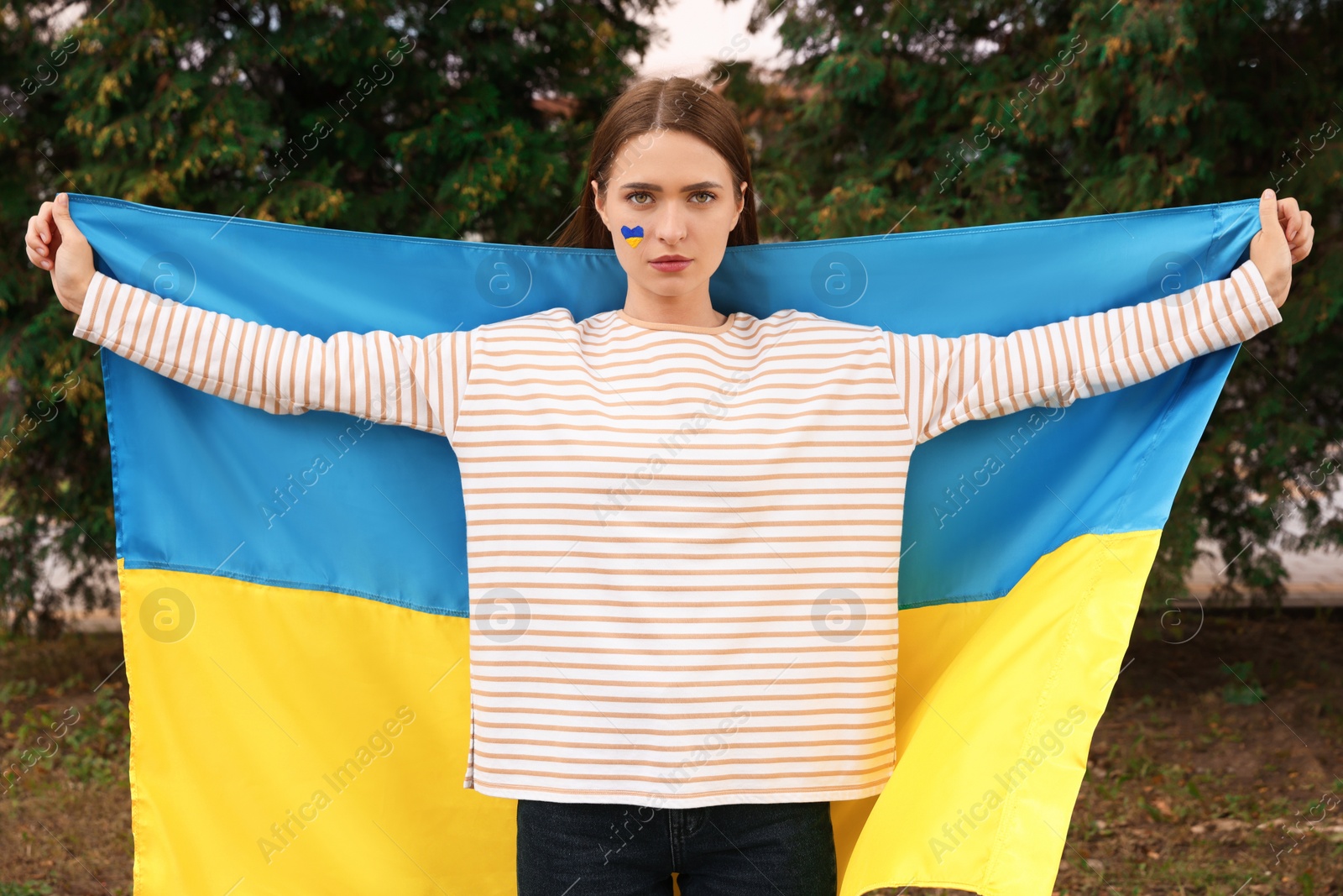 Photo of Beautiful young woman with Ukrainian flag outdoors