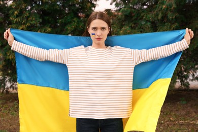 Photo of Beautiful young woman with Ukrainian flag outdoors