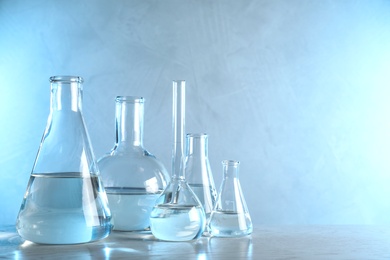Photo of Laboratory glassware with liquid samples for analysis on table against toned blue background, space for text