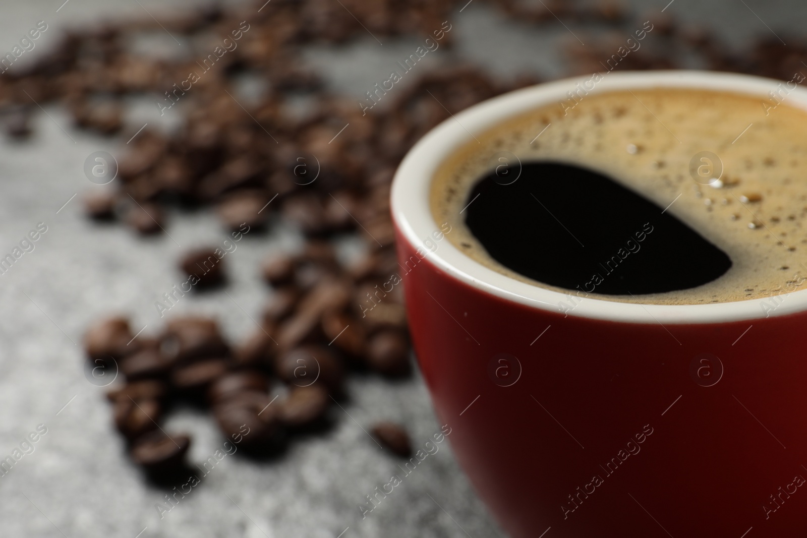 Photo of Cup of aromatic coffee and beans on grey table, closeup. Space for text