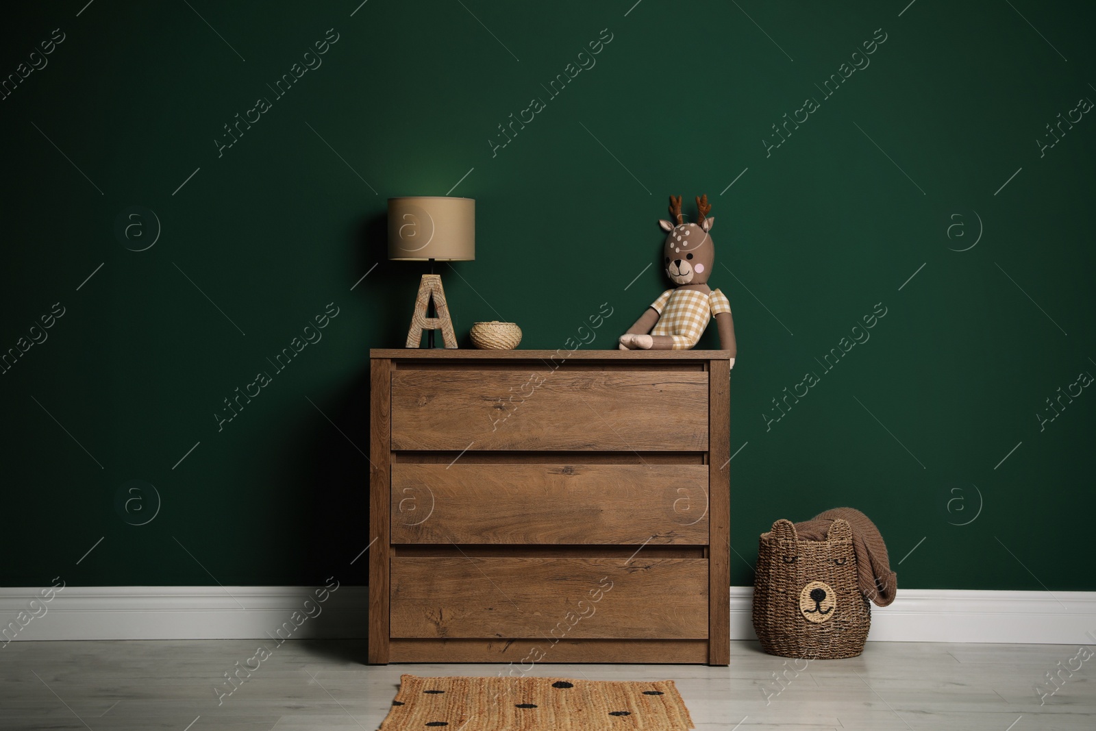 Photo of Modern wooden chest of drawers with lamp and toy near green wall indoors