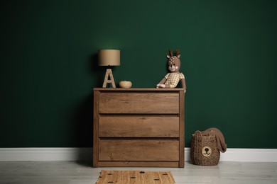 Modern wooden chest of drawers with lamp and toy near green wall indoors