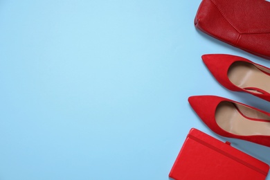 Red shoes, bag and notebook on light blue background, flat lay. Space for text