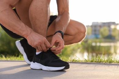Photo of Man tying shoelaces before running outdoors on sunny day, closeup. Space for text
