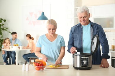 Photo of Mature couple preparing food with modern multi cooker in kitchen