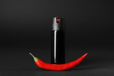 Photo of Bottle of gas spray and fresh chili pepper on black background