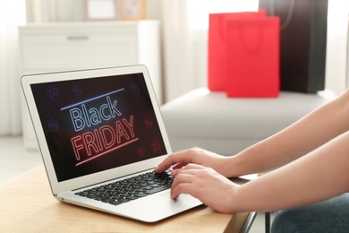 Photo of Woman using laptop with Black Friday announcement on screen at table, closeup