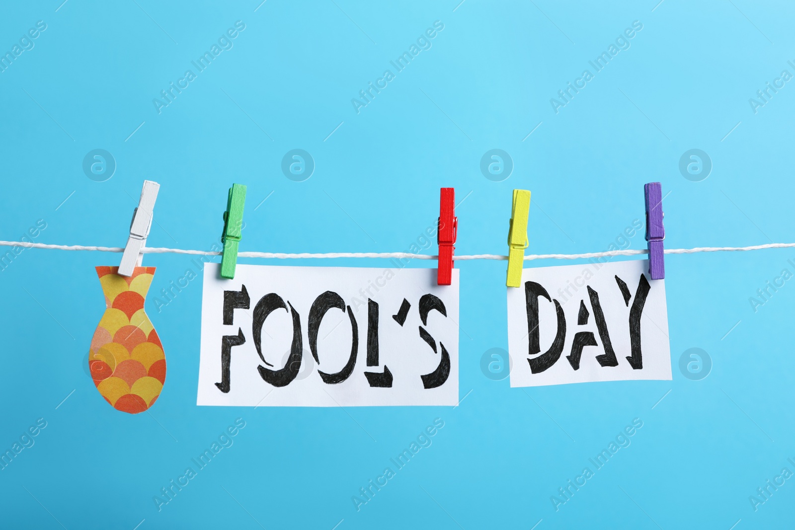 Photo of Words FOOL'S DAY and paper fish with pegs on laundry line against light blue background. April holiday