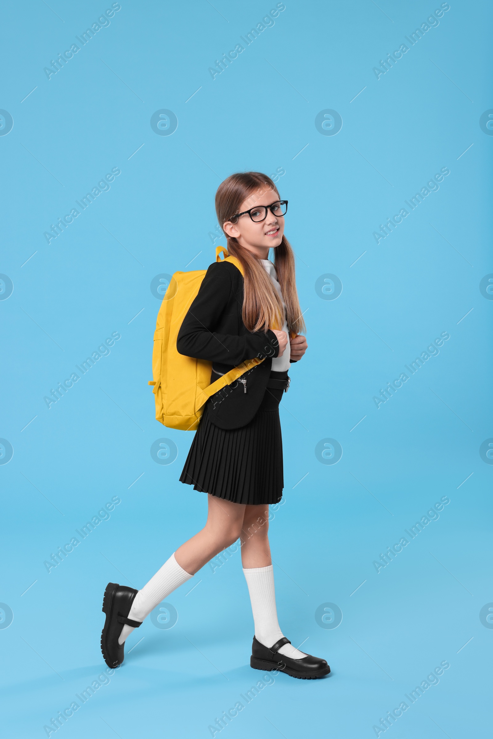 Photo of Happy schoolgirl with backpack on light blue background