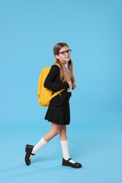 Happy schoolgirl with backpack on light blue background