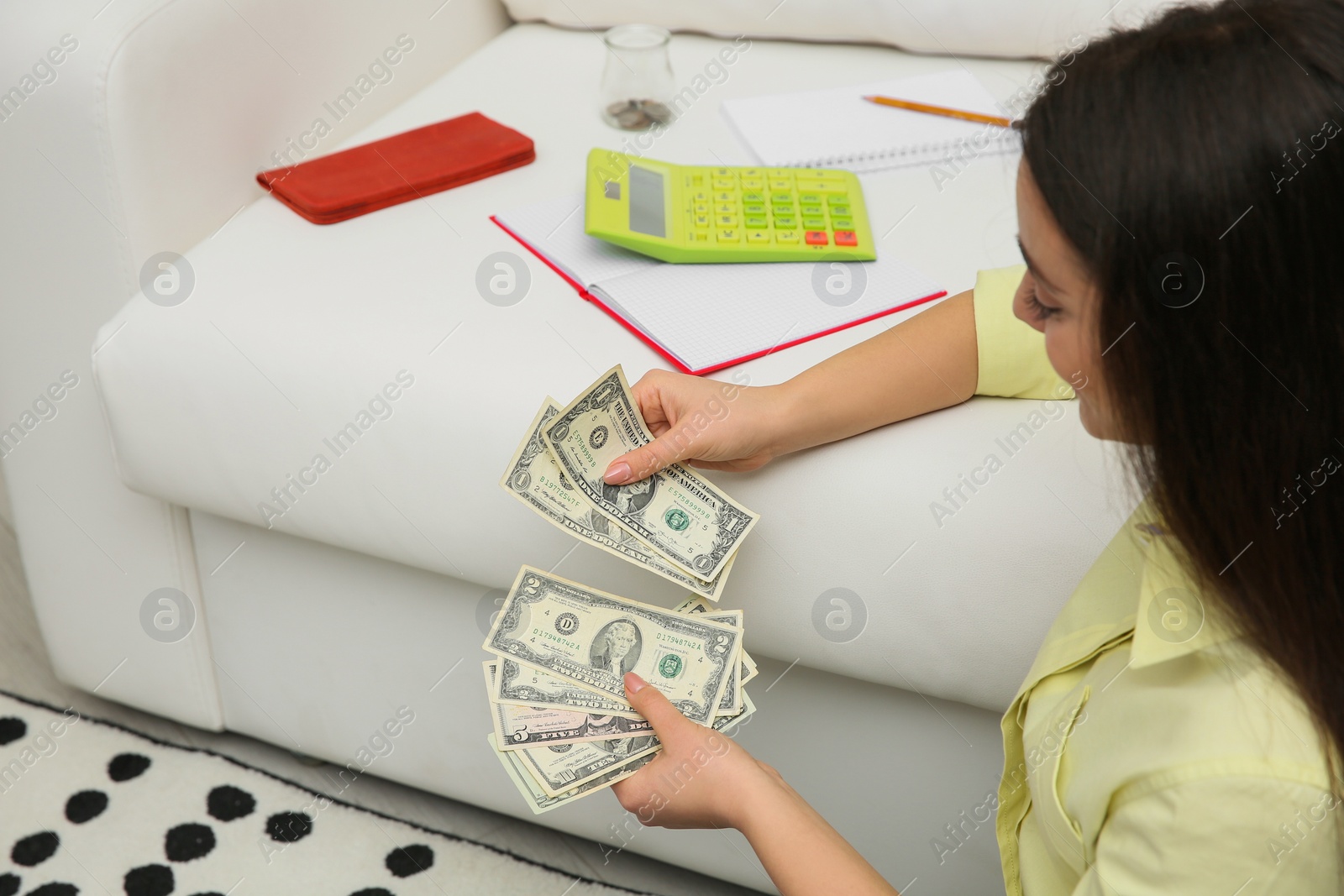 Photo of Young woman counting money near sofa at home, space for text