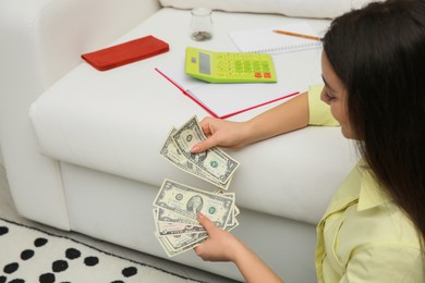 Photo of Young woman counting money near sofa at home, space for text