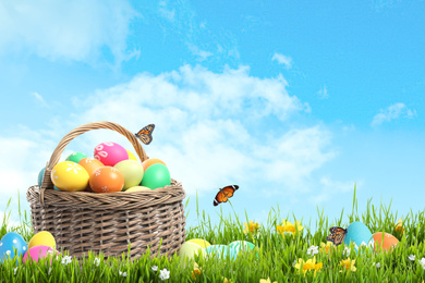 Image of Wicker basket with Easter eggs in green grass against blue sky. Space for text