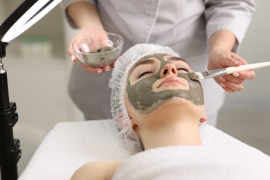 Photo of Cosmetologist applying mask on woman's face in clinic, closeup