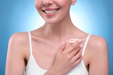 Photo of Woman with smear of body cream on her collarbone against light blue background, closeup