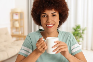 Happy young woman with cup of drink indoors