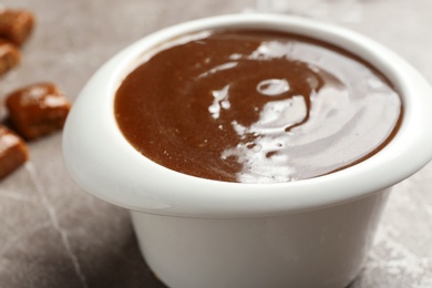Photo of Bowl with tasty caramel sauce on table, closeup
