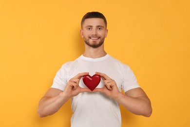 Photo of Happy volunteer holding red heart with hands on orange background