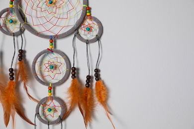 Photo of Beautiful dream catcher hanging on white wall. Space for text
