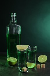 Photo of Absinthe in shot glasses, spoon, brown sugar cubes and lime on gray textured table. Alcoholic drink
