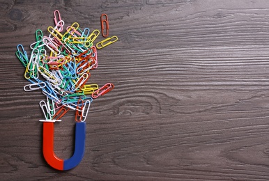 Photo of Magnet attracting paper clips on dark grey wooden background, flat lay. Space for text