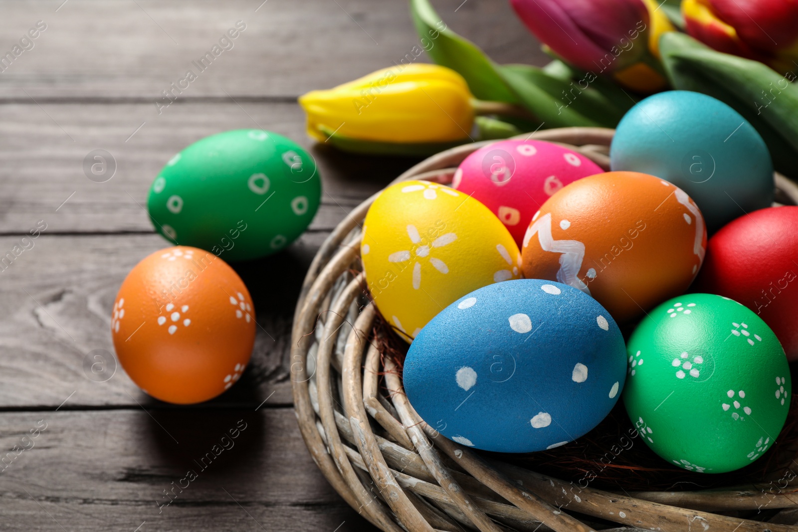 Photo of Colorful Easter eggs in decorative nest and tulips on wooden background, closeup