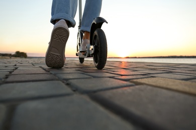 Woman riding modern kick scooter along street, closeup