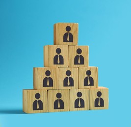 Image of Team and management concept. Pyramid of wooden cubes with human icons on light blue background