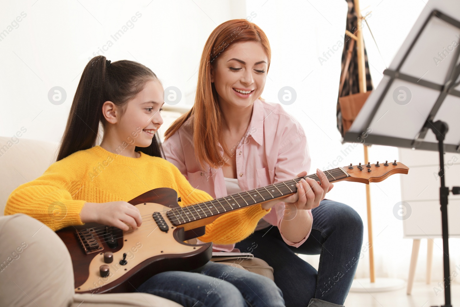 Photo of Little girl playing guitar with her teacher at music lesson. Learning notes