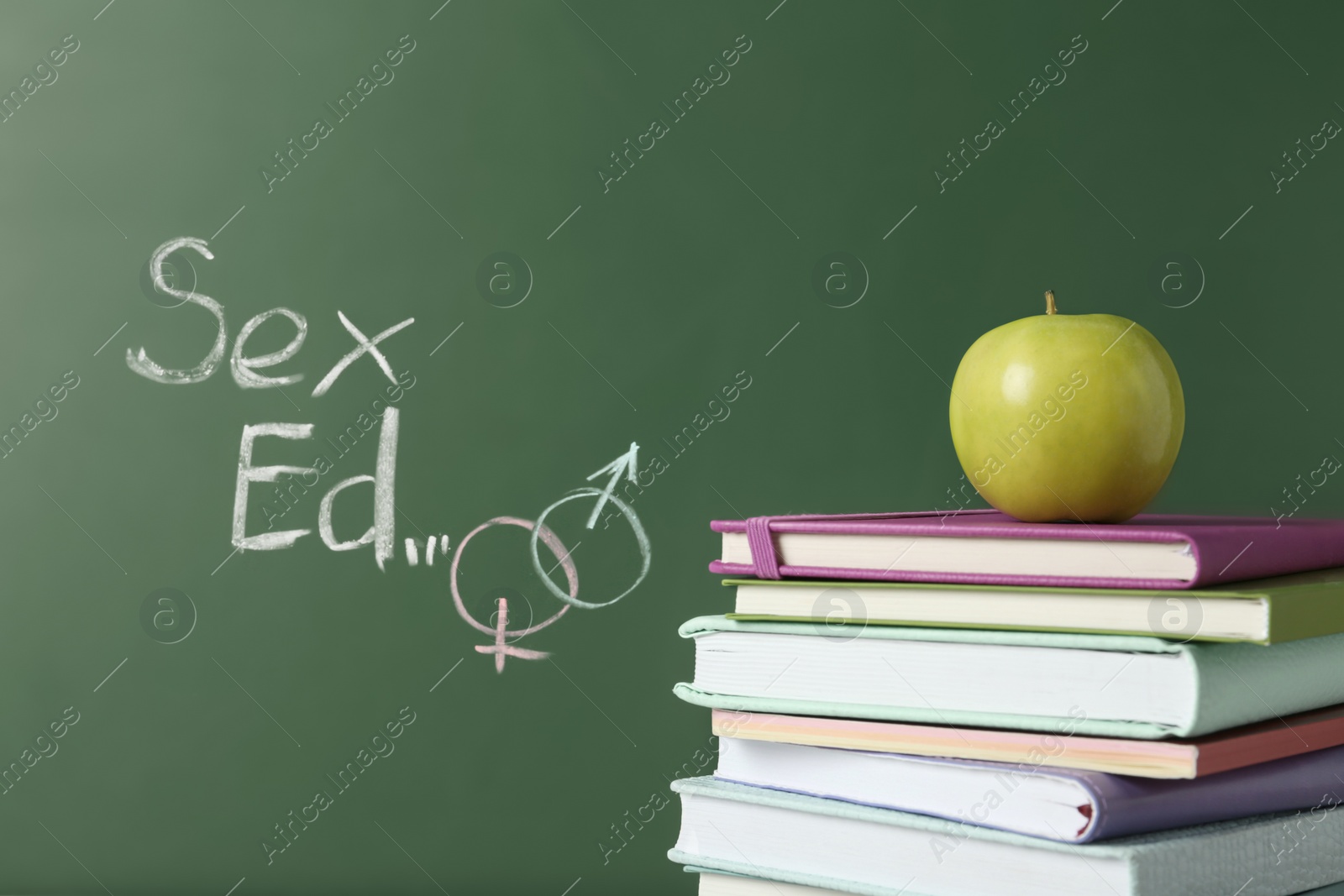 Photo of Books and apple near chalkboard with phrase "Sex ed"