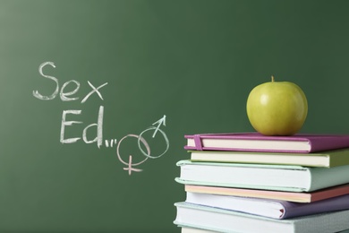 Books and apple near chalkboard with phrase "Sex ed"