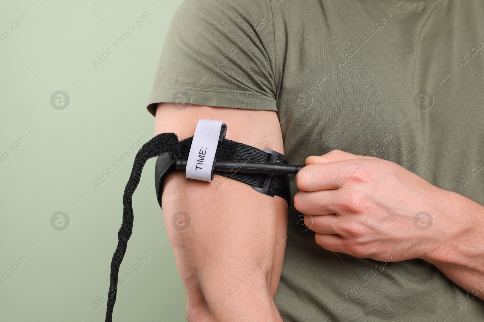 Photo of Man in military uniform applying medical tourniquet on arm against light olive background, closeup. Space for text