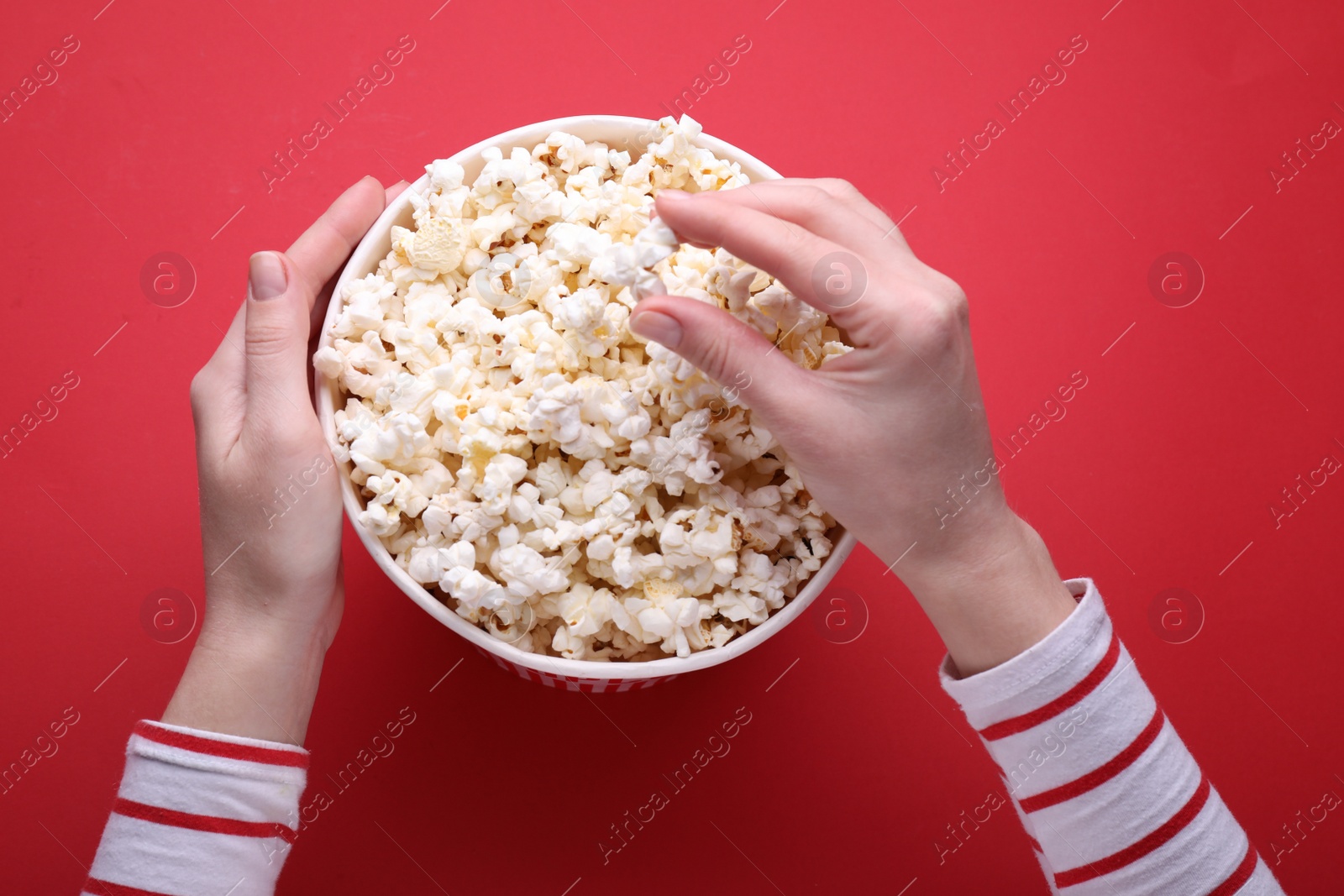 Photo of Woman taking delicious popcorn from paper bucket on red background, top view