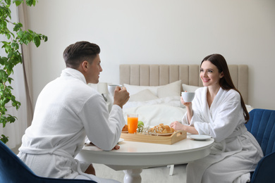 Happy couple in bathrobes having breakfast at home