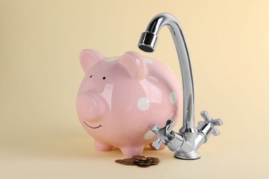 Photo of Water scarcity concept. Piggy bank, tap and coins on beige background