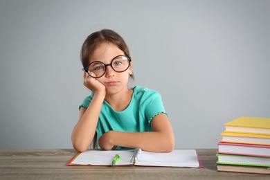 Photo of Bored little girl doing homework at table on grey background