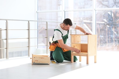 Photo of Handyman in uniform assembling furniture indoors. Professional construction tools