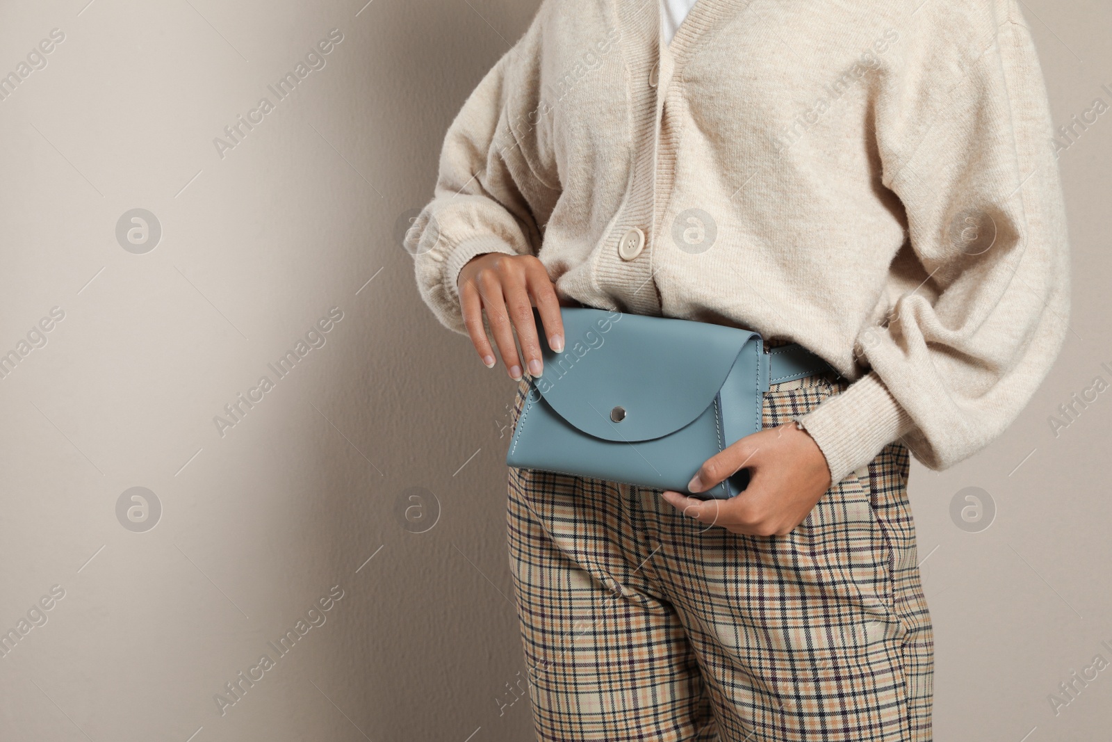 Photo of Young African American woman with stylish waist bag on beige background, closeup. Space for text