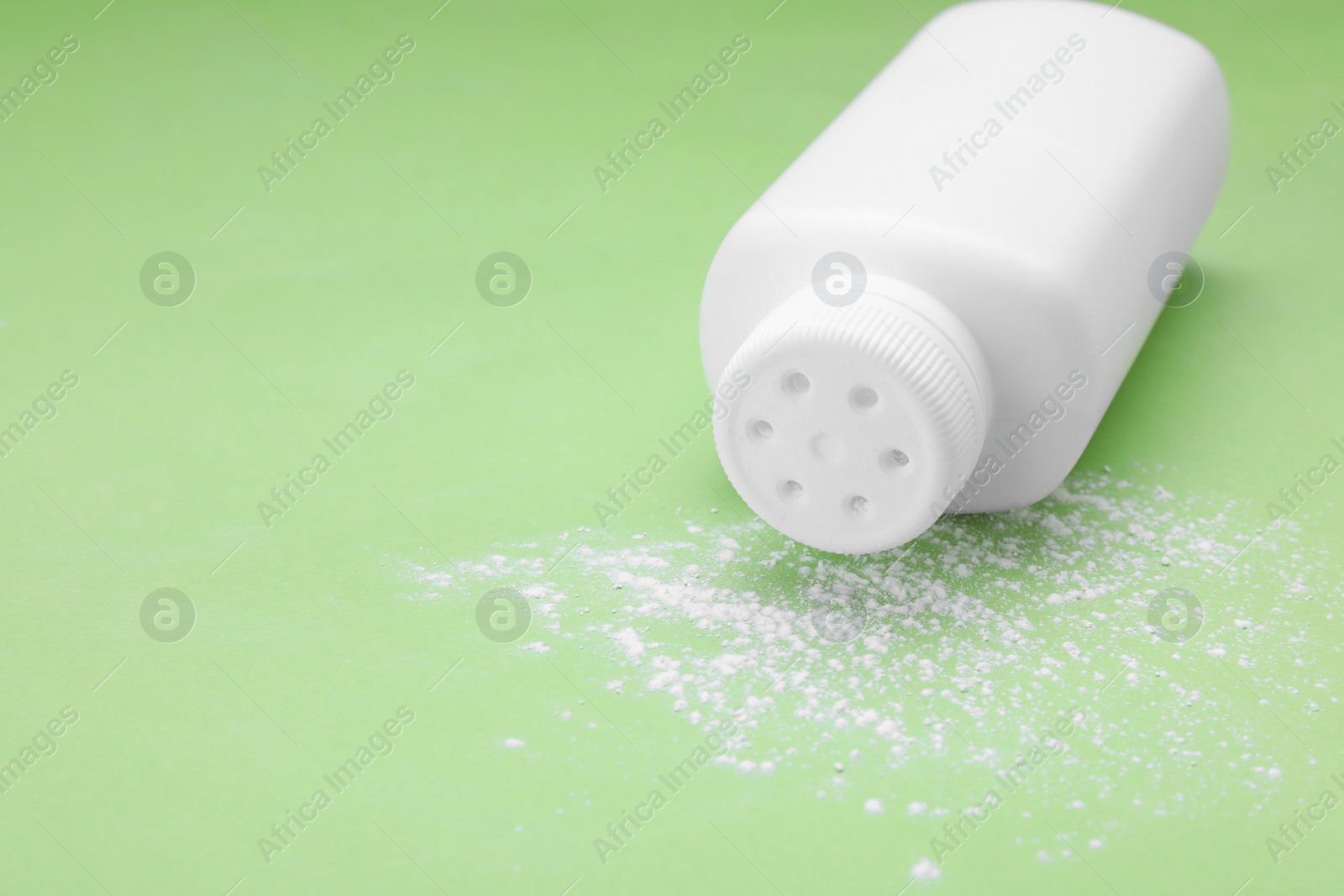 Photo of Bottle and scattered dusting powder on light green background, space for text. Baby cosmetic product