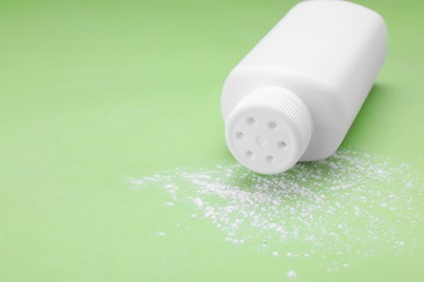 Photo of Bottle and scattered dusting powder on light green background, space for text. Baby cosmetic product