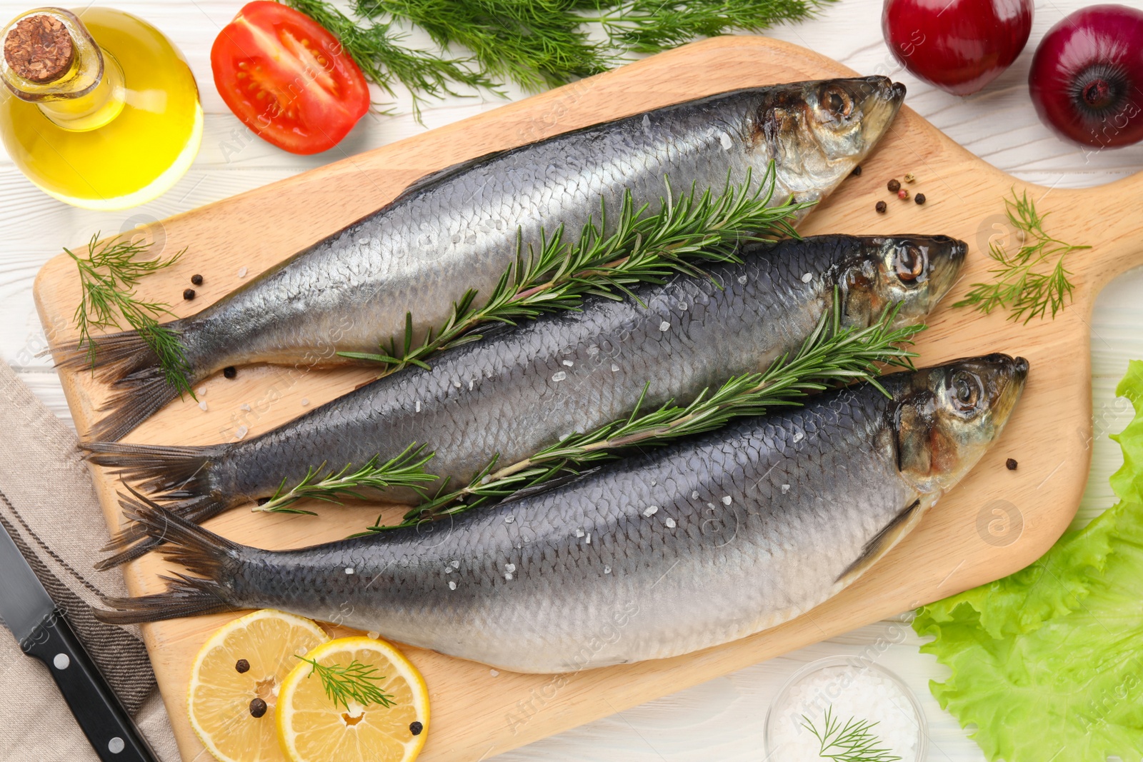 Photo of Board with delicious salted herrings and ingredients on white wooden table, flat lay