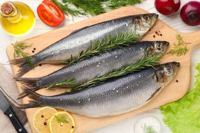 Board with delicious salted herrings and ingredients on white wooden table, flat lay