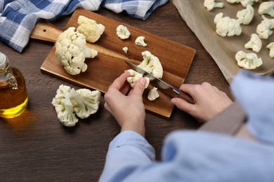 Woman cutting fresh cauliflower at wooden table, above view