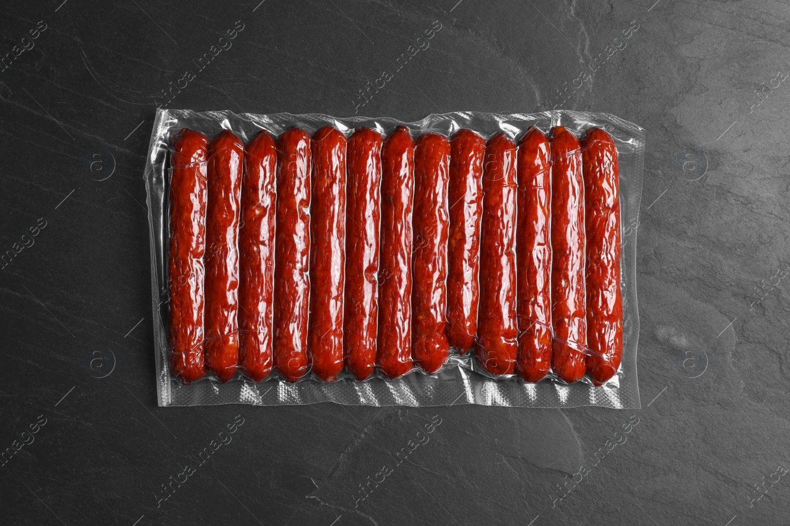 Photo of Vacuum pack of sausages on dark grey table, top view